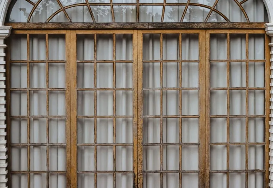 Weathered timber window with slim glazing bars and an arched fanlight above, the kind of period opening we make interior shutters for in Torquay