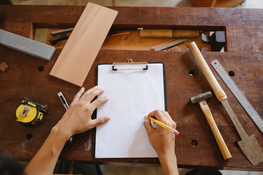 Measuring timber and sketching a cabinet layout at a workbench, the quoting stage of a Torquay boot room joinery project