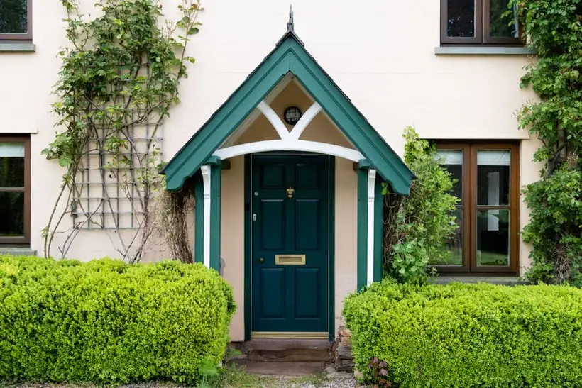 Traditional pitched timber porch over a front door on a painted cottage, the kind of covered entrance a Torquay boot room is built into