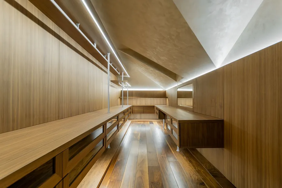 Timber-lined dressing room under a sloping ceiling lit by LED strips along the rails and shelves, as fitted in Torquay loft rooms