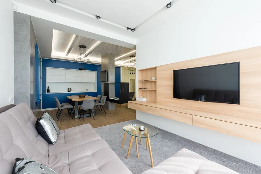 Pale timber wall panel with a flush-set television, open shelving and a floating drawer unit hiding the cables, in a modern flat