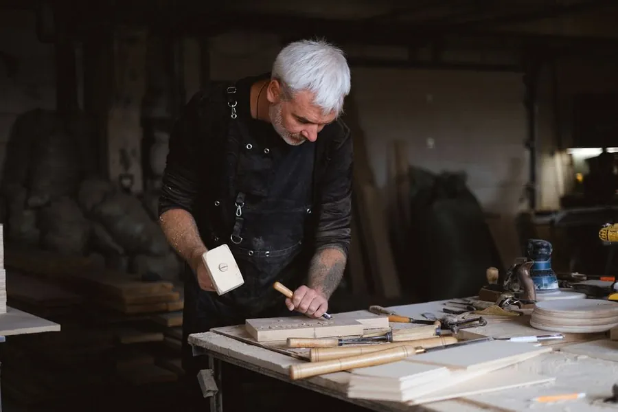 Joiner using a mallet and chisel to cut a joint in a timber board at a workshop bench, the kind of work done before anything reaches a Torquay house