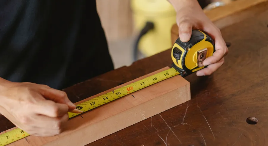 Joiner marking out a timber board with a tape measure and pencil while preparing a quote for joinery in Paignton or Brixham