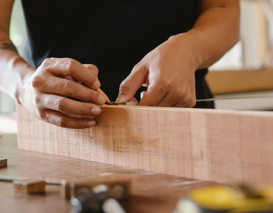 Joiner's hands measuring the width of a timber component with a steel rule and pencil