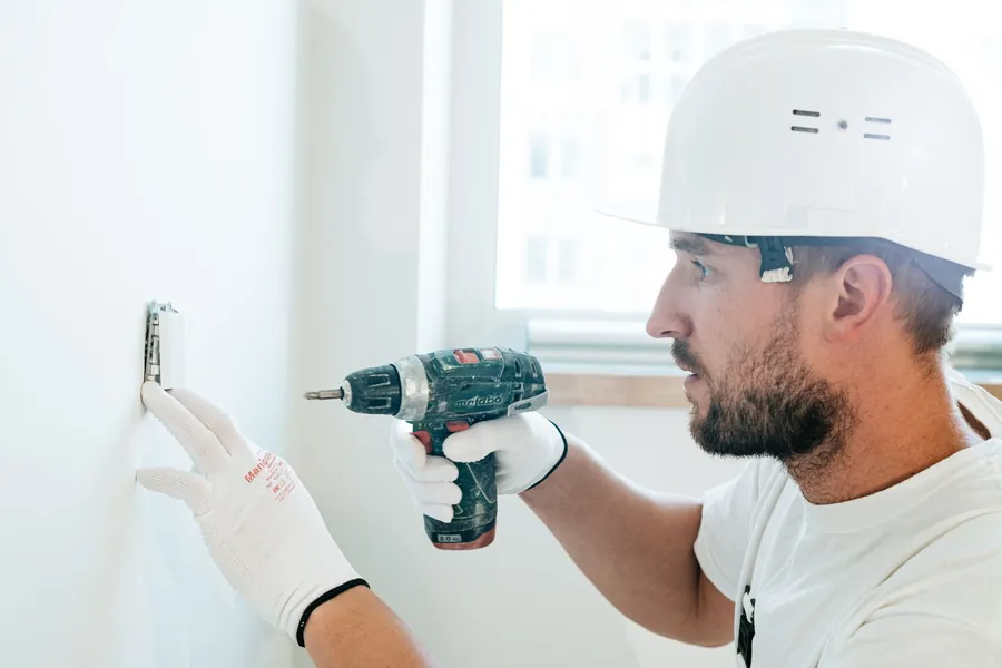 Tradesman in a hard hat drilling a fixing into a freshly plastered white wall