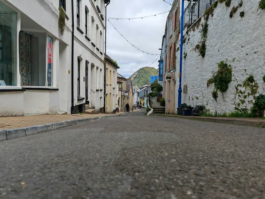 Narrow street of whitewashed and painted buildings rising towards a green hill in an old English harbour town