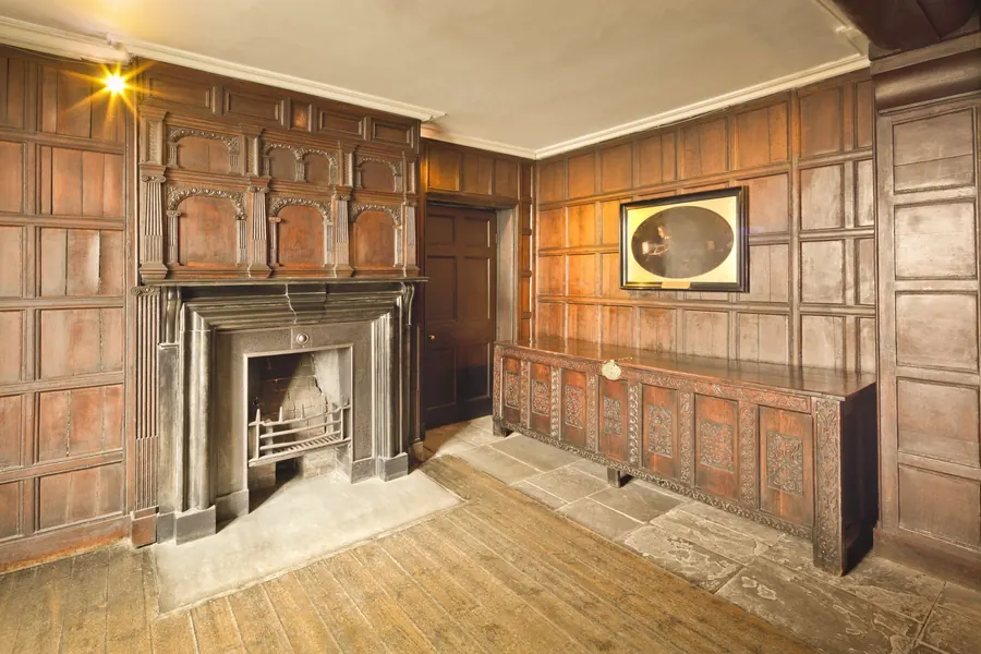Historic room lined with dark original oak panelling around a stone fireplace, the kind of early joinery that needs repair rather than replacement