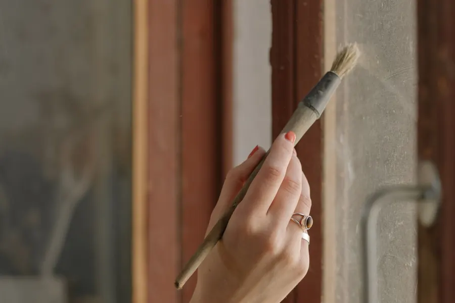 Brush applying paint to the edge of a timber window frame, sealing the joinery against damp in a Torbay home