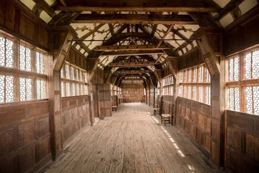 Long timber gallery with panelled walls, exposed roof trusses and rows of leaded windows
