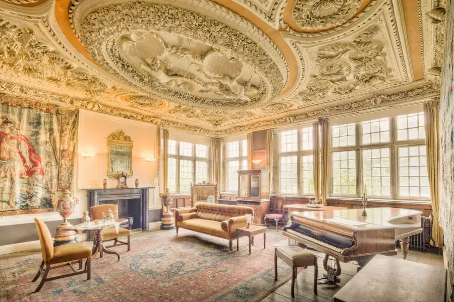 Panelled room with an ornate moulded plaster ceiling, tall mullioned windows and period furniture