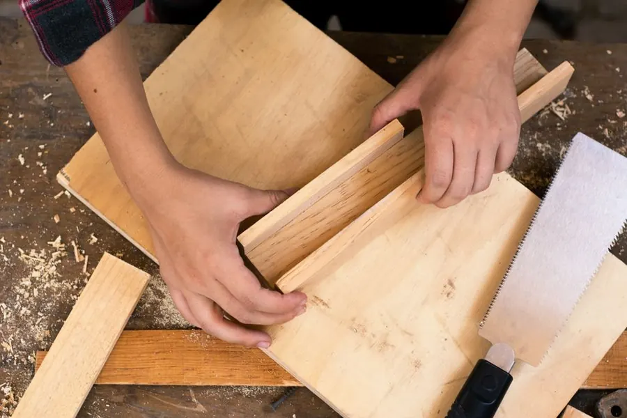 Carpenter cutting a length of timber moulding to fit, the bench work behind matched skirting and architrave