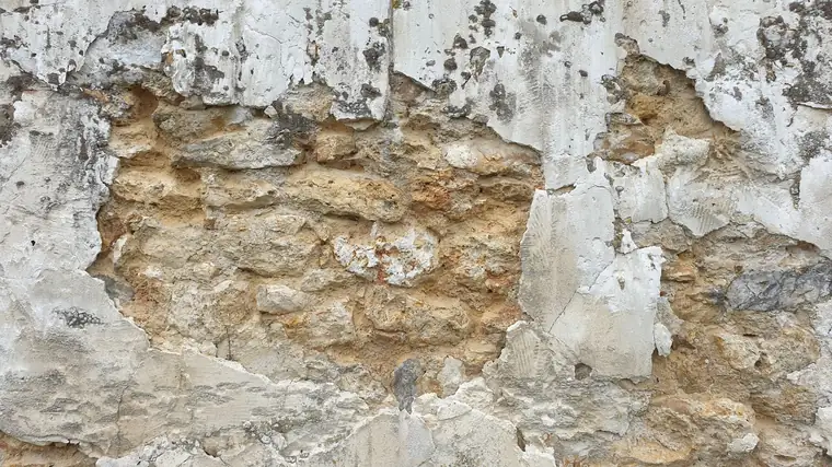 Rubble stone wall showing through broken lime plaster, the kind of solid wall found behind the plaster in many older Torquay houses