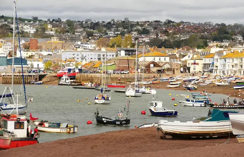 Small boats pulled up on a red-sand estuary beach with painted houses and a hillside town behind