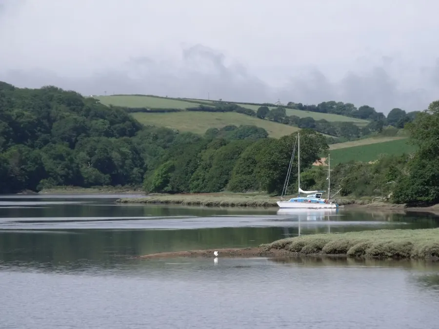 Yacht moored on a calm tidal river with wooded hills and green fields beyond