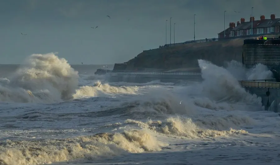 Waves breaking over a seafront wall below coastal houses, the salt spray that reaches external timber joinery in Torbay