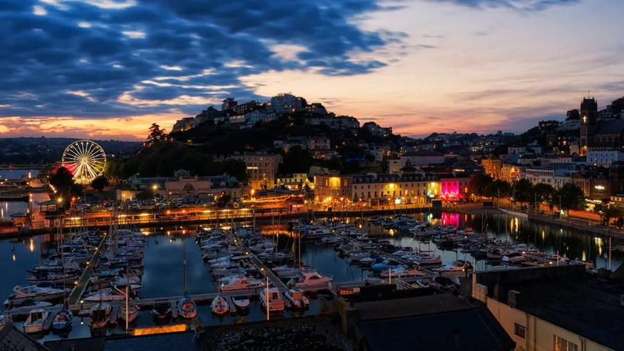 Torquay harbour and seafront buildings lit up in the evening, where homes see damp salt air off the bay for much of the year