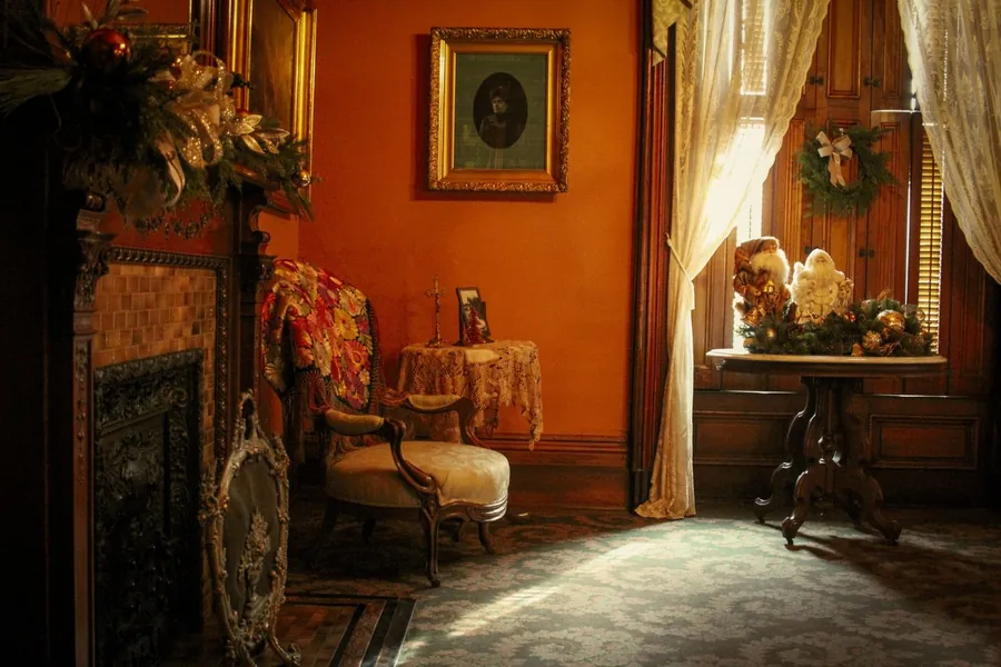 Victorian sitting room with a cast iron fireplace, armchair and lace curtains at a tall window
