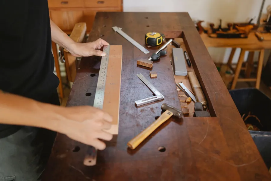 Joiner measuring a timber component on a workshop bench surrounded by hand tools, where a walk-in wardrobe for a Torquay house is made