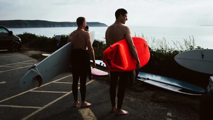 Surfers with boards and wetsuits at an English coastal car park, the sort of beach kit Torbay boot room joinery has to store