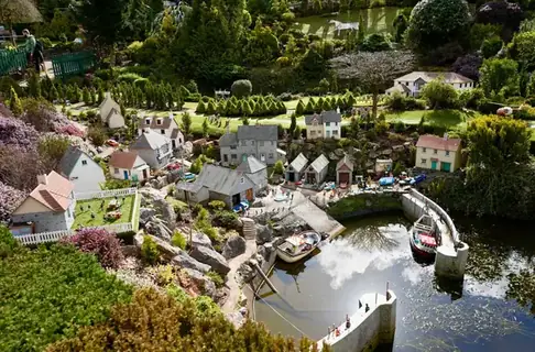 Miniature model houses, a pond and tiny boats among clipped green planting in a model village