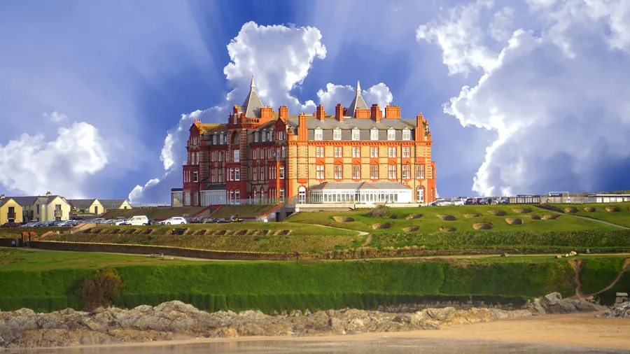 A large red brick Victorian hotel standing on a clifftop lawn under a big sky