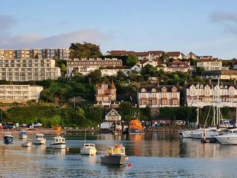 Terraces of houses stepping up the hill above small boats moored in Brixham harbour