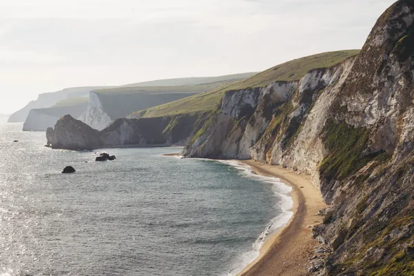 Pale cliffs and green headland dropping to a curved bay of calm sea