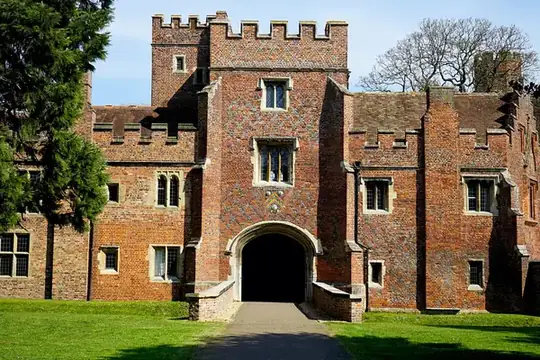 A medieval gatehouse with crenellated towers and an arched entrance behind a lawn