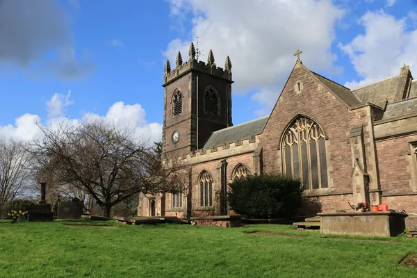 A stone parish church with a square tower behind a grassy churchyard