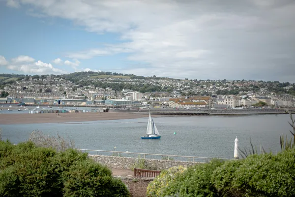 A seaside town spread along the shore across calm bay water, with a sailing boat
