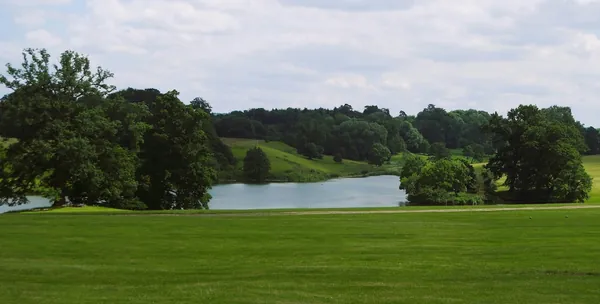 Open parkland lawn sloping down to a lake ringed by mature trees
