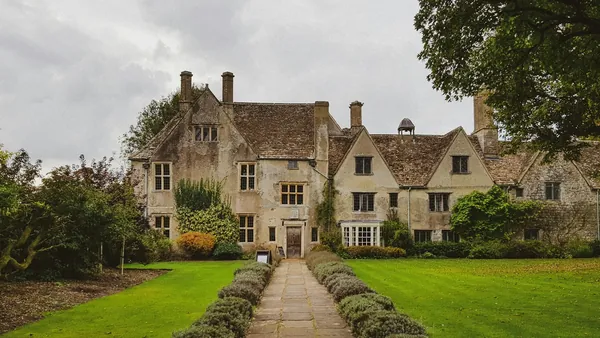 A gabled stone manor house reached by a straight path across the lawn