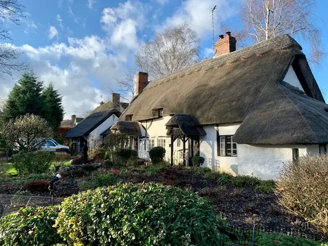 A whitewashed cottage with a deep thatched roof behind a planted garden