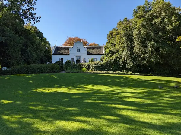A white country house among mature trees above a sunlit lawn