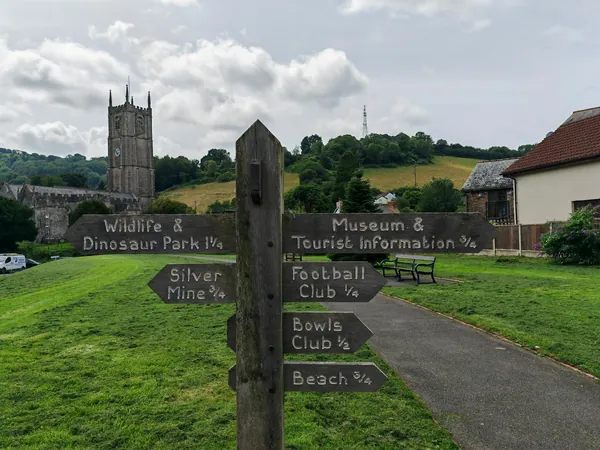A wooden fingerpost on a village green with a church tower behind