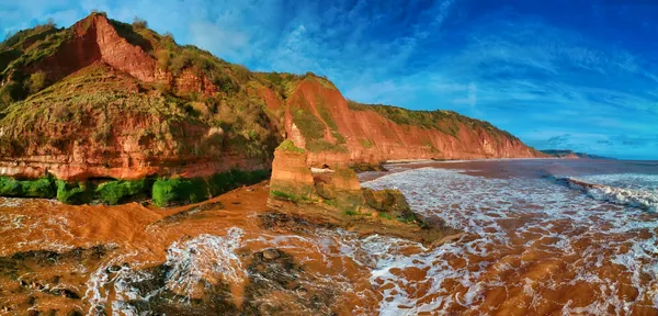 Red sandstone cliffs topped with green growth above a rocky shore