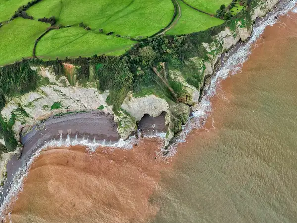 A small cove with red sandy shore and pale cliffs seen from the air