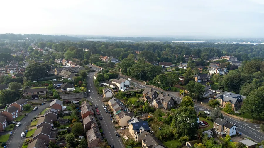 Houses and gardens set among trees on the edge of a village, seen from above
