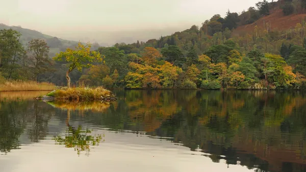 A calm lake reflecting wooded slopes in autumn colour