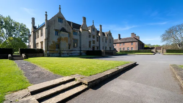 An old stone manor house with gables and mullioned windows behind a lawn