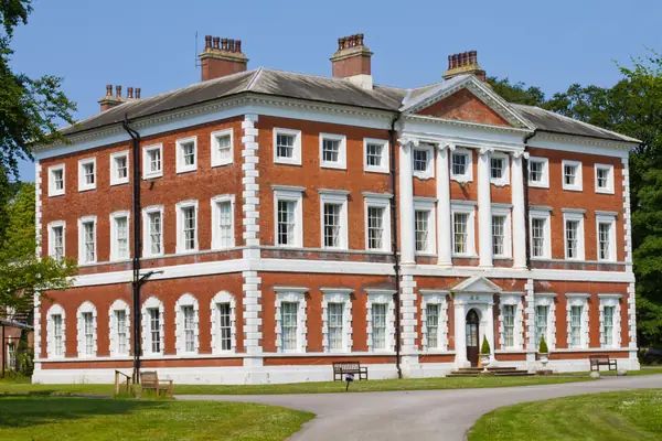 A red brick house with white window surrounds above a sloping lawn