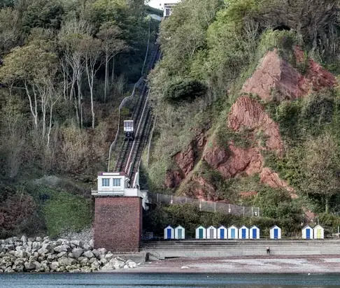 A cliff railway track running down a steep red cliff face through trees to the lower station