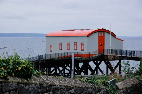A red-roofed waterside building on a timber jetty above the shore