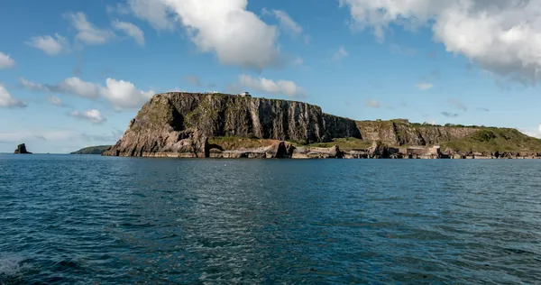 A steep-sided rocky island in calm sea under a summer sky