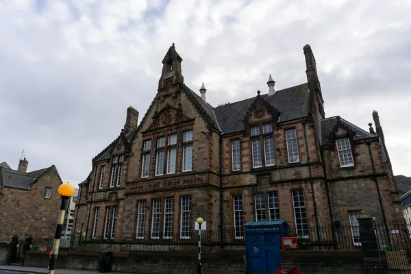 A gabled Victorian stone building with tall mullioned windows on a street corner