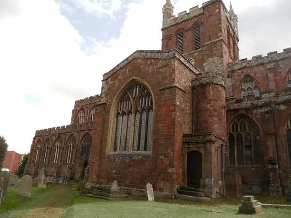 A red stone church with a tall tower and traceried windows