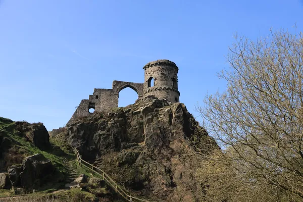 A small stone ruin on top of a rocky crag under a blue sky