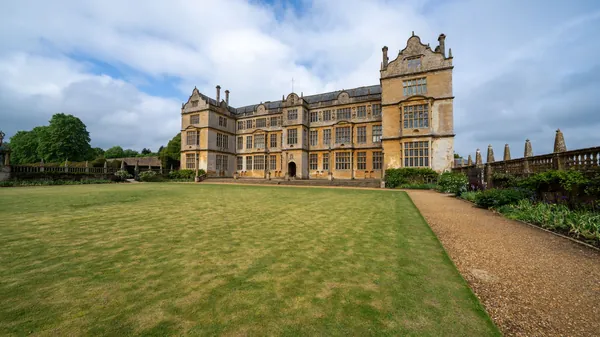 A historic stone hall behind wide formal lawns and a gravel path