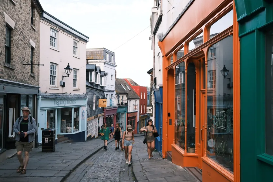 Shoppers walking up a sloping street of painted shopfronts