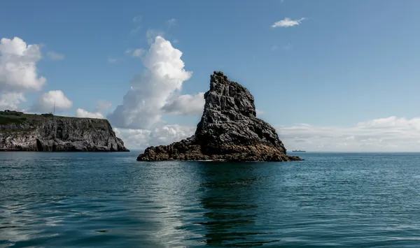 A jagged rock stack and low cliffs rising from calm blue water